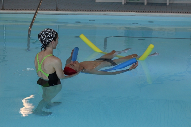 Młody mężczyzny rehabilitujący się na basenie, obok asystuje kobieta.