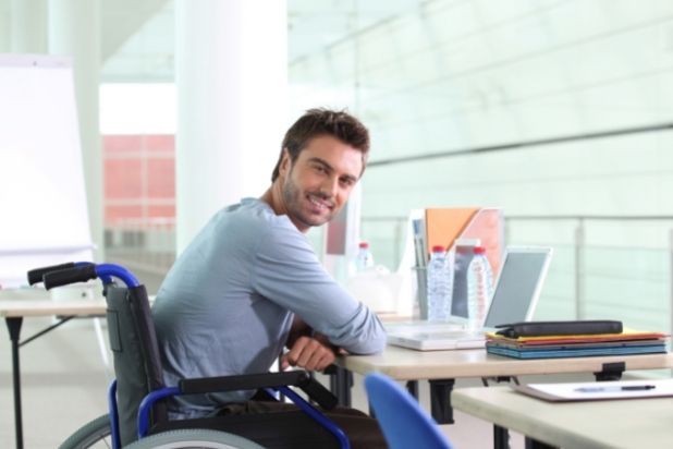 Uśmiechnięty mężczyzna na wózku podczas pracy biurowej.