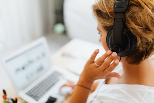 Fragmentaryczna postać kobiety pracującej przed komputerem, z słuchawkami na uszach.