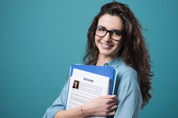 Młoda, uśmiechnięta kobieta w okularach. Trzymająca w ręku dokumenty, m.in. CV