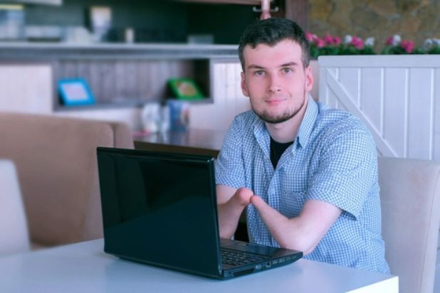 Młody mężczyzna bez rąk siedzi przed laptopem.
