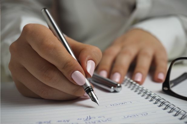 dłonie kobiety piszącej w zeszycie długopisem